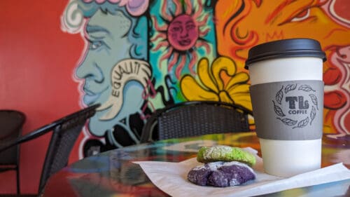 A table at Tree Lounge set with to-go coffee and colorful cookies with a vibrant mural in the background
