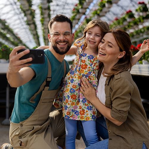 Family taking a selfie in a greenhouse with colorful flowers in the background.